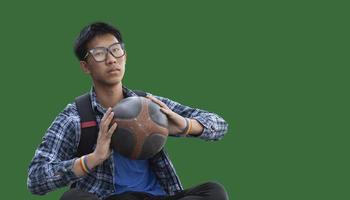 Isolated asian male teenager in plaid shirt holding old and training basketball in hand with clipping paths. photo