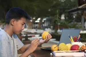 Asian boy holds paintbrush and yellow bell pepper which molded from plaster, coloring and painting outer surface with same color during his free times, idea for hobby and art learning. photo