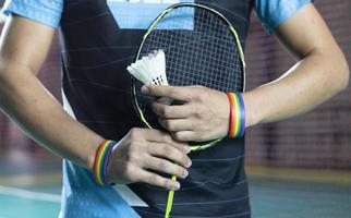 Badminton player wears rainbow wristbands and holding racket and white shuttlecock in front of the net before serving it to player in another side of the court, concept for LGBT people activities. photo