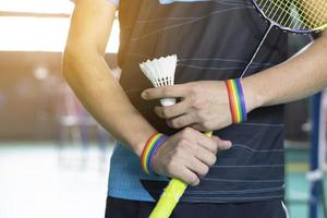 Badminton player wears rainbow wristbands and holding racket and white shuttlecock in front of the net before serving it to player in another side of the court, concept for LGBT people activities. photo