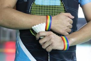 Badminton player wears rainbow wristbands and holding racket and white shuttlecock in front of the net before serving it to player in another side of the court, concept for LGBT people activities. photo