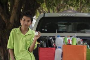 Asian boys are separating garbages and putting them into the boxes in front of them near building, soft and selective focus, environment care, community service and summer vacation activities concept. photo