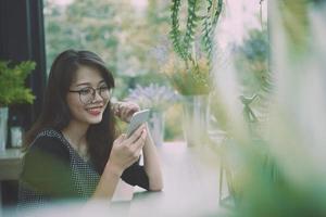 hermosa asiático mas joven mujer leyendo mensaje en inteligente teléfono y sonriente con felicidad cara foto