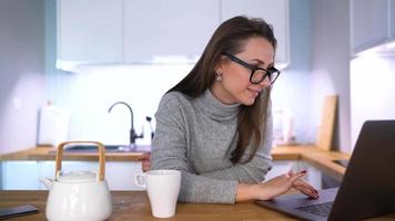 caucasiano mulher tendo café da manhã dentro a cozinha e usando uma computador portátil video