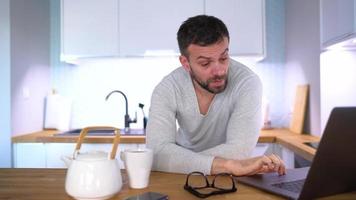 barbado hombre teniendo desayuno en el cocina y utilizando un ordenador portátil video