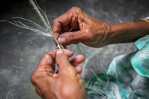 un antiguo años mujer es haciendo en su flaco manos un cuerda desde el plátano árbol fibra a madhupur, tangail, bangladesh foto