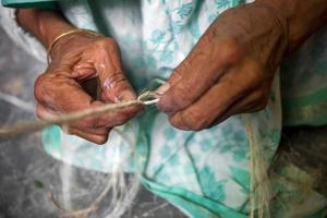 un antiguo años mujer es haciendo en su flaco manos un cuerda desde el plátano árbol fibra a madhupur, tangail, bangladesh foto