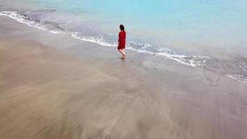 Aerial view of a man in red shorts rotates around himself stretching arms to the sides on the beach with black sand video