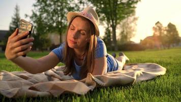 Mädchen Herstellung ein Selfie Lügen Nieder auf ein Decke im das Park beim Sonnenuntergang video