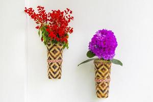 Bamboo flower vase with red lilac flowers hanging on the white wall. Isolated background. photo