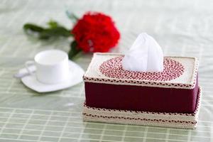 Deep red Handmade fiber Napkin box on the dining table with a red flower and a white tea-cup. Tissue paper box on restaurant. photo