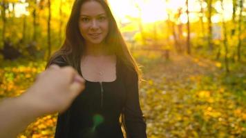 Beautiful girl holds the hand of her boyfriend and follows him through the yellow autumn forest. Slow motion video