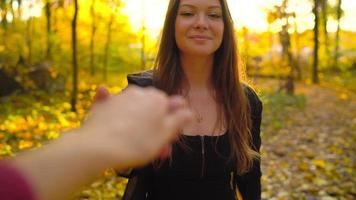 hermosa niña sostiene el mano de su novio y sigue él mediante el amarillo otoño bosque. lento movimiento video