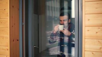 hombre Bebiendo té o café cerca el ventana y mirando mediante el vaso video