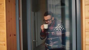 hombre Bebiendo té o café cerca el ventana y mirando mediante el vaso video