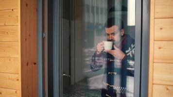 hombre Bebiendo té o café cerca el ventana y mirando mediante el vaso video