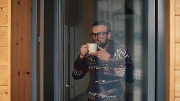 hombre Bebiendo té o café cerca el ventana y mirando mediante el vaso video