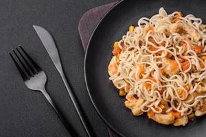 Delicious noodles with chicken and vegetables or udon on a black ceramic plate photo