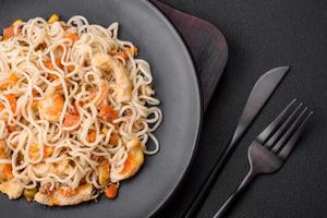 Delicious noodles with chicken and vegetables or udon on a black ceramic plate photo
