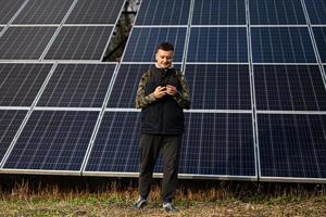 hombre con móvil teléfono en el antecedentes de solar paneles eco energía. foto