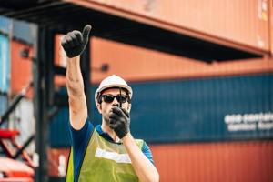 Logistics, shipping and construction worker using walkie talkie in shipyard. Transportation engineer on smartphone in delivery, freight and international distribution business in container yard photo