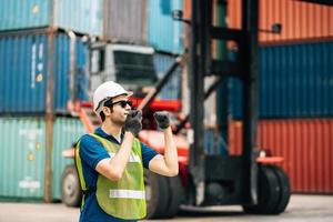 Logistics, shipping and construction worker using walkie talkie in shipyard. Transportation engineer on smartphone in delivery, freight and international distribution business in container yard photo