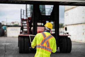 African technician dock worker in protective safety jumpsuit uniform and with hardhat and use digital tablet at cargo container shipping warehouse. transportation import,export logistic industrial photo