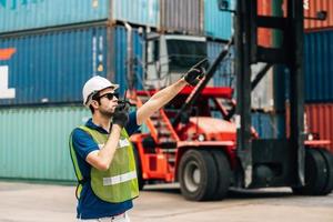 Logistics, shipping and construction worker using walkie talkie in shipyard. Transportation engineer on smartphone in delivery, freight and international distribution business in container yard photo