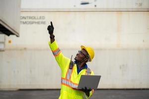 African technician dock worker in protective safety jumpsuit uniform and with hardhat and use digital tablet at cargo container shipping. transportation concept.,import,export logistic industrial photo