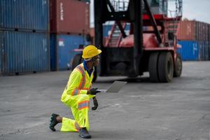 African technician dock worker in protective safety jumpsuit uniform and with hardhat and use digital tablet at cargo container shipping warehouse. transportation import,export logistic industrial photo