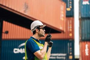 Logistics, shipping and construction worker using walkie talkie in shipyard. Transportation engineer on smartphone in delivery, freight and international distribution business in container yard photo