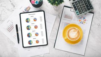 Tablet with charts and reports on office desk workplace. Top view flat lay. photo