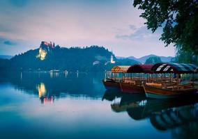 Three lake tour boats standing on famous bled lake with castle on the background and island church. Peaceful relaxing holiday destination in Slovenia.Triglav national park photo