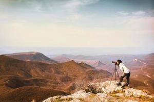 Young passionate attractive caucasian hipster woman content creator photographing mountains with red girly DSLR camera on tripod photo