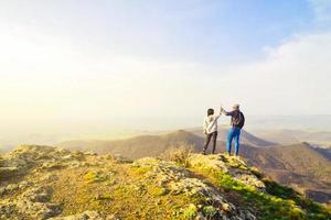 Caucasian young travelous couple enjoy mountain top viewpoint panorama together after reaching top. Hands up clapping for success, freedom and happy travels Holiday vacation photo