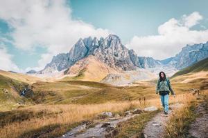 frente contento hembra caucásico mujer caminante camina en ruta en juta Valle con Kazbegi Cáucaso montañas paisaje. Kazbegi nacional parque explorar trekking concepto foto