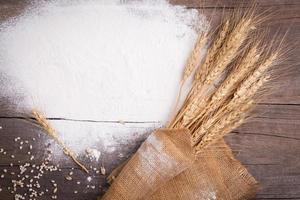 harina y orejas de trigo, cebada, cocinando, pan, y galletas fueron arreglado en el de madera mesa antecedentes en un rústico cocina. parte superior vista. foto