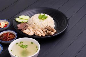 Hainanese chicken rice on a black wooden table background steamed chicken rice with chicken soup, sauces condiments Asian food Thailand China Singapore, top view photo