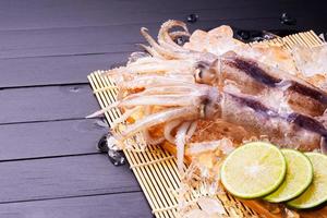 Raw squid on ice with lemon garlic spice salad on black wooden table background, fresh squid for cooked food at a kitchen restaurant or seafood market photo