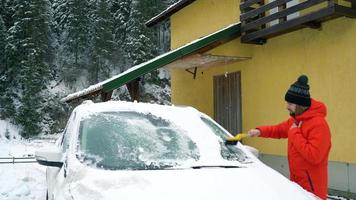 homme nettoie le voiture de le neige près le sien maison video