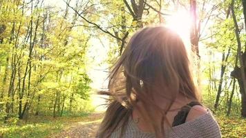 retrato de un hermosa sonriente niña en un sombrero con un amarillo arce hoja en el primer plano en el otoño bosque. lento movimiento video