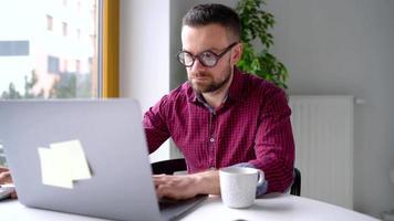 Bearded man having breakfast in the kitchen and using a laptop video