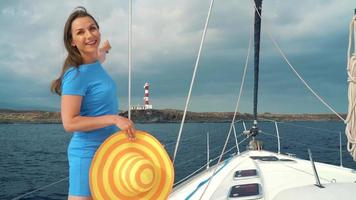 Woman in a yellow hat and blue dress girl rests aboard a yacht near the lighthouse on summer season at ocean video