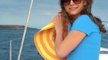 donna nel un' giallo cappello e blu vestito ragazza riposa a bordo un' yacht vicino il faro su estate stagione a oceano video