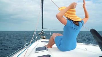 Woman in a yellow hat and blue dress girl rests aboard a yacht near the lighthouse on summer season at ocean video