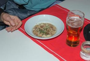 Bowl of hot chicken broth with noodles on a white background. A glass of fresh foamy beer. photo