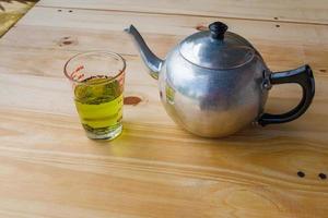 A cup with green tea and teapot on white wooden table background. photo