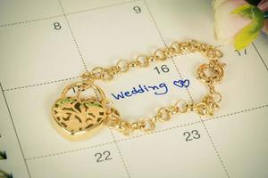 word wedding on calendar and gold bracelet with heart photo