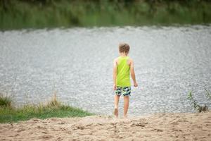 Child on the banks of the river rear view. A boy by the pond. photo