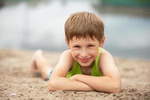 pequeño alegre niño en el arena cerca el agua. retrato de un chico en verano ropa en el playa. foto